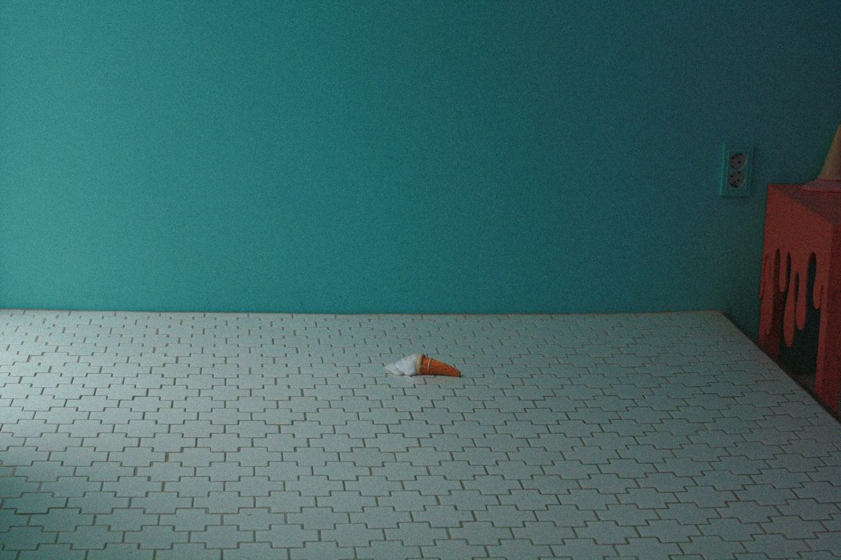 A kitchen floor and countertop arranged with a gel bait placed along a cabinet hinge, a small bait station near the baseboard, a dust applicator aimed into a wall crack, and an aerosol can set aside near an unopened fogger canister